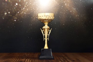 Altın kupanın loş görüntüsü ahşap masa ve koyu arkaplan üzerinde, soyut parlak ışık ile