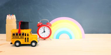 Eğitim ve okul konseptine geri dönüş. Ahşap masasında mezuniyet şapkası olan sarı otobüs.