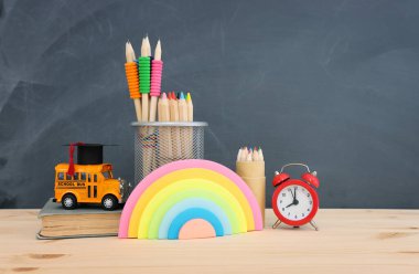 Eğitim ve okul konseptine geri dönüş. Sarı otobüs, mezuniyet şapkası ve tahta masa üzerindeki kalemler.