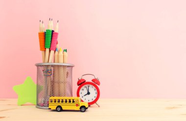 Eğitim ve okul konseptine geri dönüş. Pastel pembe karatahtanın önündeki ahşap masanın üzerine kırtasiye malzemesi.