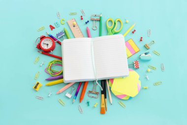 Okul konseptine geri dönelim. Pastel mavi arkaplan üzerinde açık boş defter ve öğrenci kırtasiyesinin en üst görünümü