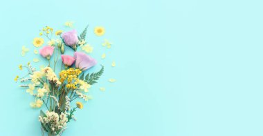 Pastel mavi arkaplan üzerinde pembe, sarı ve mor çiçek kompozisyonu.