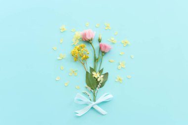 Pastel mavi arkaplan üzerinde pembe, sarı ve mor çiçek kompozisyonu.