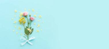 Pastel mavi arkaplan üzerinde pembe, sarı ve mor çiçek kompozisyonu.