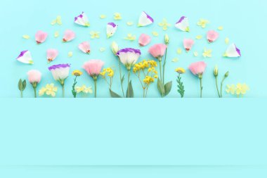 Pastel mavi arkaplan üzerinde pembe, sarı ve mor çiçek kompozisyonu.