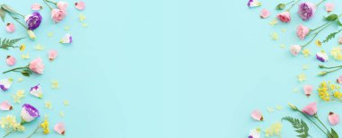 Pastel mavi arkaplan üzerinde pembe, sarı ve mor çiçek kompozisyonu.