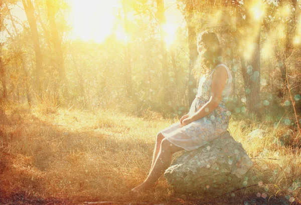 Surreal blurred background of young woman sitting on the tsone in forest — Stock Photo, Image