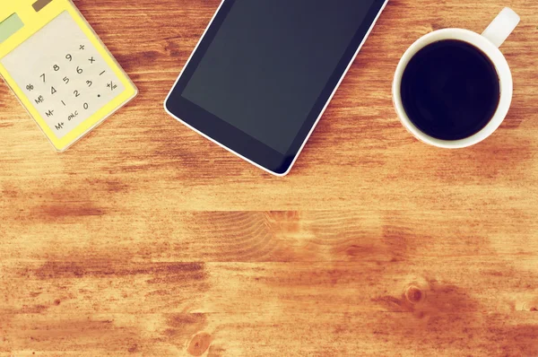 Vista superior do tablet, xícara de café e calculadora sobre fundo de mesa texturizado de madeira. imagem é tonificada . — Fotografia de Stock