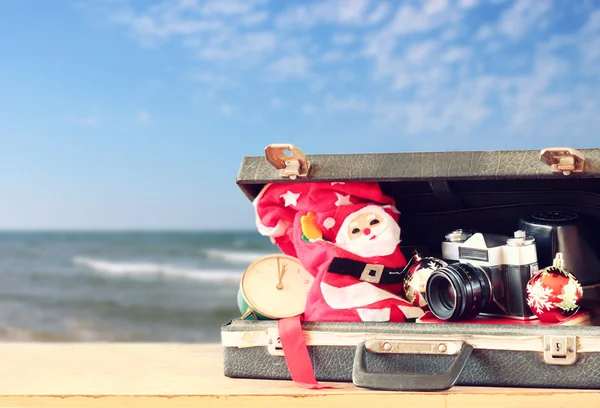 Open briefcase with christmas decorations and camera in front of beach view. christmas holiday concept. — Stock Photo, Image