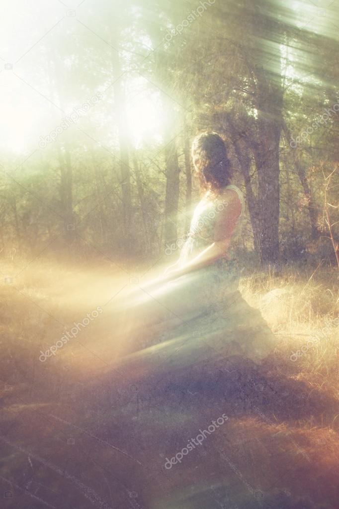 Surreal blurred background of young woman sitting on the tsone in forest