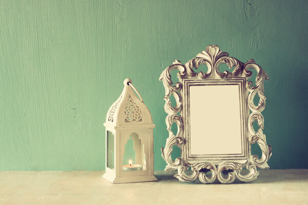 Low key image of vintage antique classical frame and Lantern on wooden table. filtered image