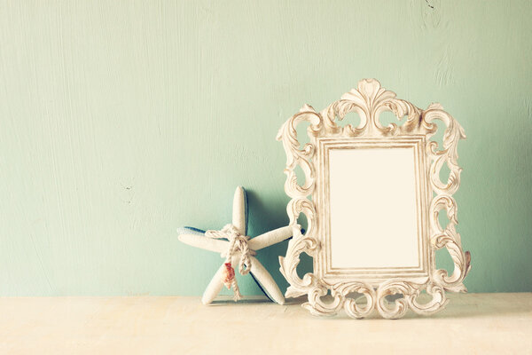 Low key image of vintage antique classical frame and starfish on wooden table. filtered image