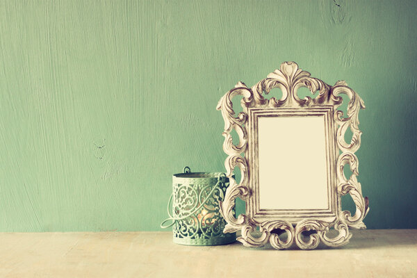 Low key image of vintage antique classical frame and white lantern on wooden table. filtered image