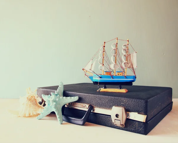 Old Vintage sutcase with toy boat' starfish and seashell  on wooden board. travel and voyage concept. retro filtered image — Stock Photo, Image