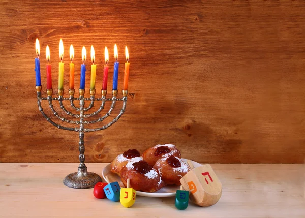 Jewish holiday Hanukkah with menorah, doughnuts and wooden dreidels (spinning top).