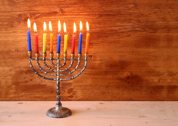 Low key image of jewish holiday Hanukkah background with menorah Burning candles over wooden background