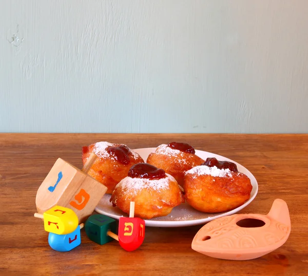 Donuts caseros y dreidels de madera (spinning top) para las vacaciones judías del hanukkah sobre tabla de madera —  Fotos de Stock