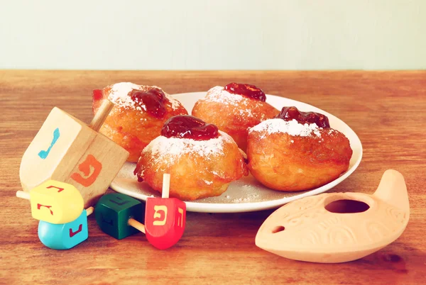 Donuts caseiros e dreidels de madeira (top giratório) para férias judaicas hanukkah sobre mesa de madeira. imagem retro filtrada — Fotografia de Stock