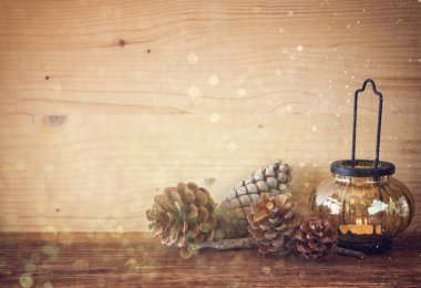 Yanma ile vintage fener mum, çam kozalakları ahşap masa ve parlak ışıklar arka plan üzerinde. Filtre uygulanmış görüntü