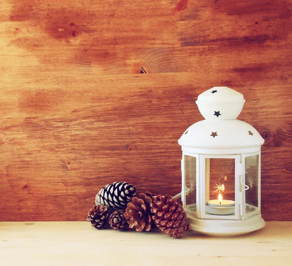 Linterna Vintage con vela ardiente y conos de pino sobre mesa de madera. imagen filtrada —  Fotos de Stock