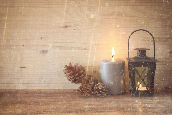 Vintage Lantern with burning candles, pine cones on wooden table and glitter lights background. filtered image — Stock Photo, Image