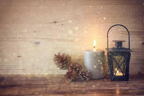 Vintage Lantern with burning candles, pine cones on wooden table and glitter lights background. filtered image — Stock Photo, Image