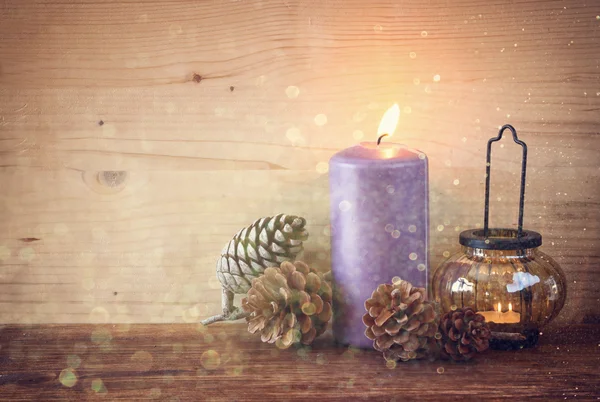 Lanterna vintage com velas em chamas, cones de pinho na mesa de madeira e luzes de brilho de fundo. imagem filtrada — Fotografia de Stock