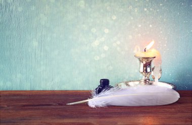 Düşük anahtar görüntü eski ahşap masa beyaz tüy, InkWell, kaydırma ve mum ve parlak ışıklar arka plan