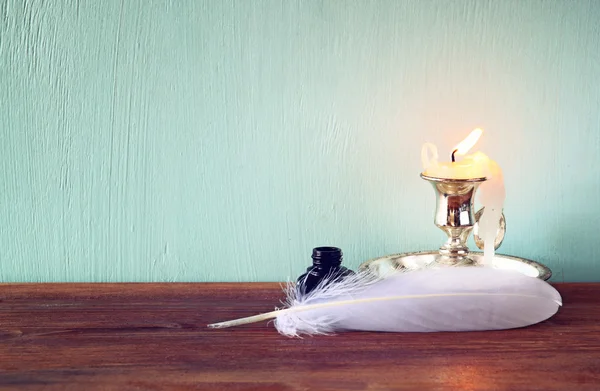 Image basse de plumes blanches, encrier et bougie sur une vieille table en bois — Photo