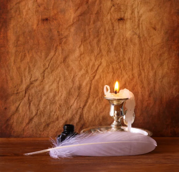 Image basse de plumes blanches, encrier et bougie allumée sur une table en bois — Photo