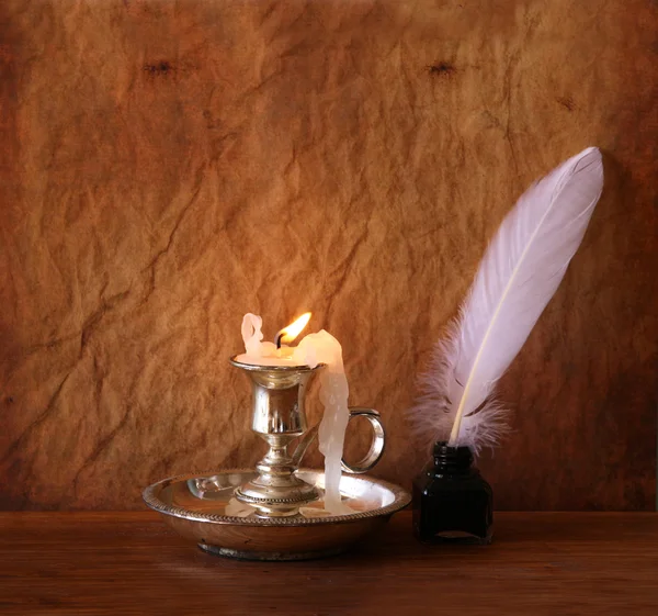 Low key image of white Feather, inkwell and burning candle on a wooden table — Stock Photo, Image