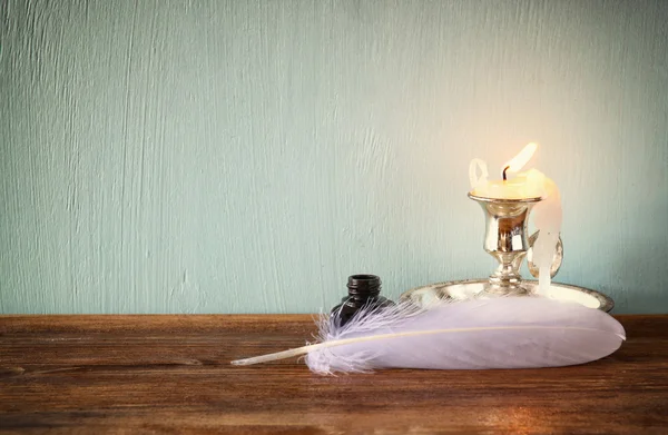 Image basse de plumes blanches, encrier et bougie allumée sur une table en bois — Photo