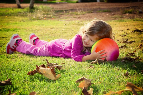 Lilla vackra flicka leker med sin boll på gräset i parken. filtrerade bilden — Stockfoto