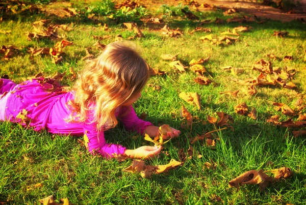 Маленька мила дівчинка грає зі своїм м'ячем на траві в парку. фільтроване зображення — стокове фото
