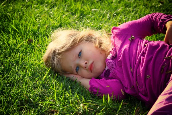 Lilla vackra flicka leker med sin boll på gräset i parken. filtrerade bilden — Stockfoto