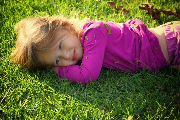 Lilla vackra flicka leker med sin boll på gräset i parken. filtrerade bilden — Stockfoto