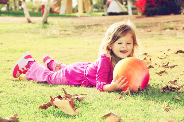 Kicsi szép lány játszik vele labdát a füvön, a parkban. szűrt kép — Stock Fotó