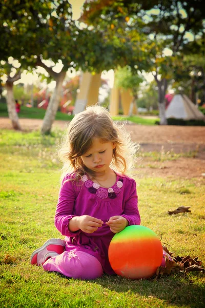 Lilla vackra flicka som leker på gräset i parken. filtrerade bilden — Stockfoto