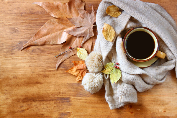 Top view of Cup of black coffee with autumn leaves, a warm scarf on wooden background. filreted image