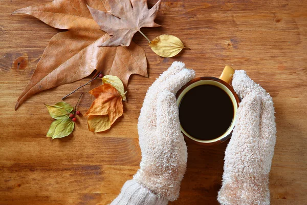 Vista superior de las manos femeninas con un café caliente, sobre fondo de madera — Foto de Stock