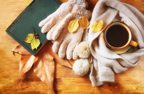 Vue du dessus de la tasse de café noir avec des feuilles d'automne, un foulard chaud et un vieux livre sur fond en bois. image filtrée — Photo