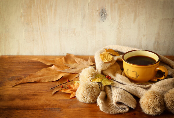 Top view of Cup of black coffee with autumn leaves, a warm scarf on wooden background. filreted image