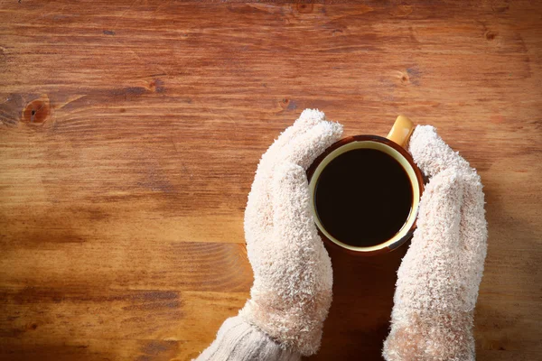 Vista superior das mãos femininas com um café quente, em fundo de madeira — Fotografia de Stock