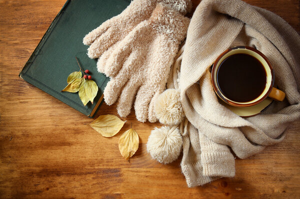 Top view of Cup of black coffee with autumn leaves, a warm scarf and old book on wooden background. filreted image