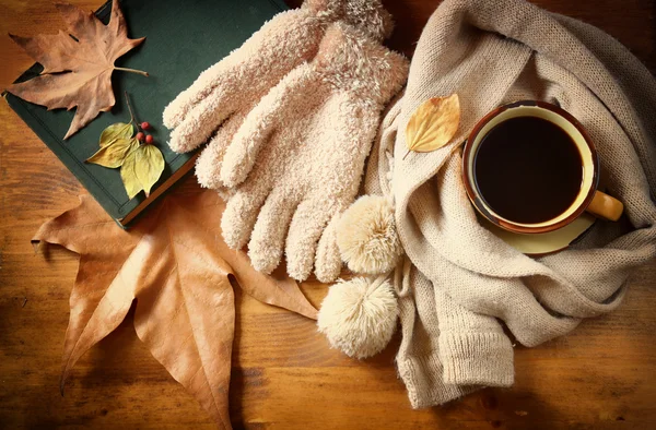 Vue du dessus de la tasse de café noir avec des feuilles d'automne, un foulard chaud et un vieux livre sur fond en bois. image filtrée — Photo