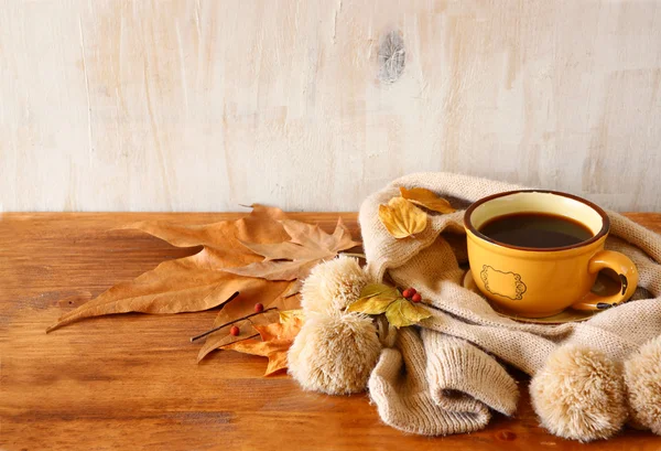 Vista superior de la taza de café negro con hojas de otoño, una bufanda caliente sobre fondo de madera. imagen filtrada — Foto de Stock