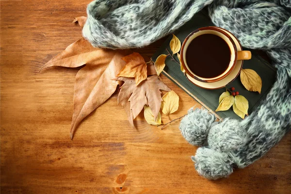 Vue du dessus de la tasse de café noir avec des feuilles d'automne, un foulard chaud et un vieux livre sur fond en bois. image filtrée — Photo