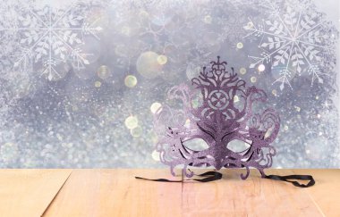 Kar tanesi bindirmeleri ahşap masa ve glitter zemin üzerine gizemli Venedik maskeli balo maskesi