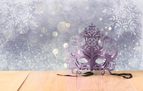Mysterious Venetian masquerade mask on wooden table and glitter background with snowflake overlays — Stock Photo, Image