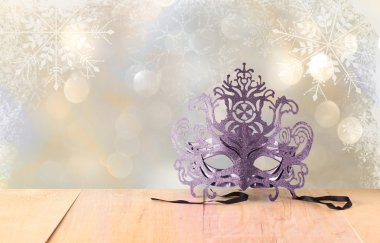 Kar tanesi bindirmeleri ahşap masa ve glitter zemin üzerine gizemli Venedik maskeli balo maskesi